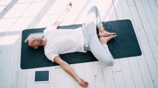 A man lies on his back performing butterfly pose. His knees are bent, feet touching, arms splayed out by his sides.