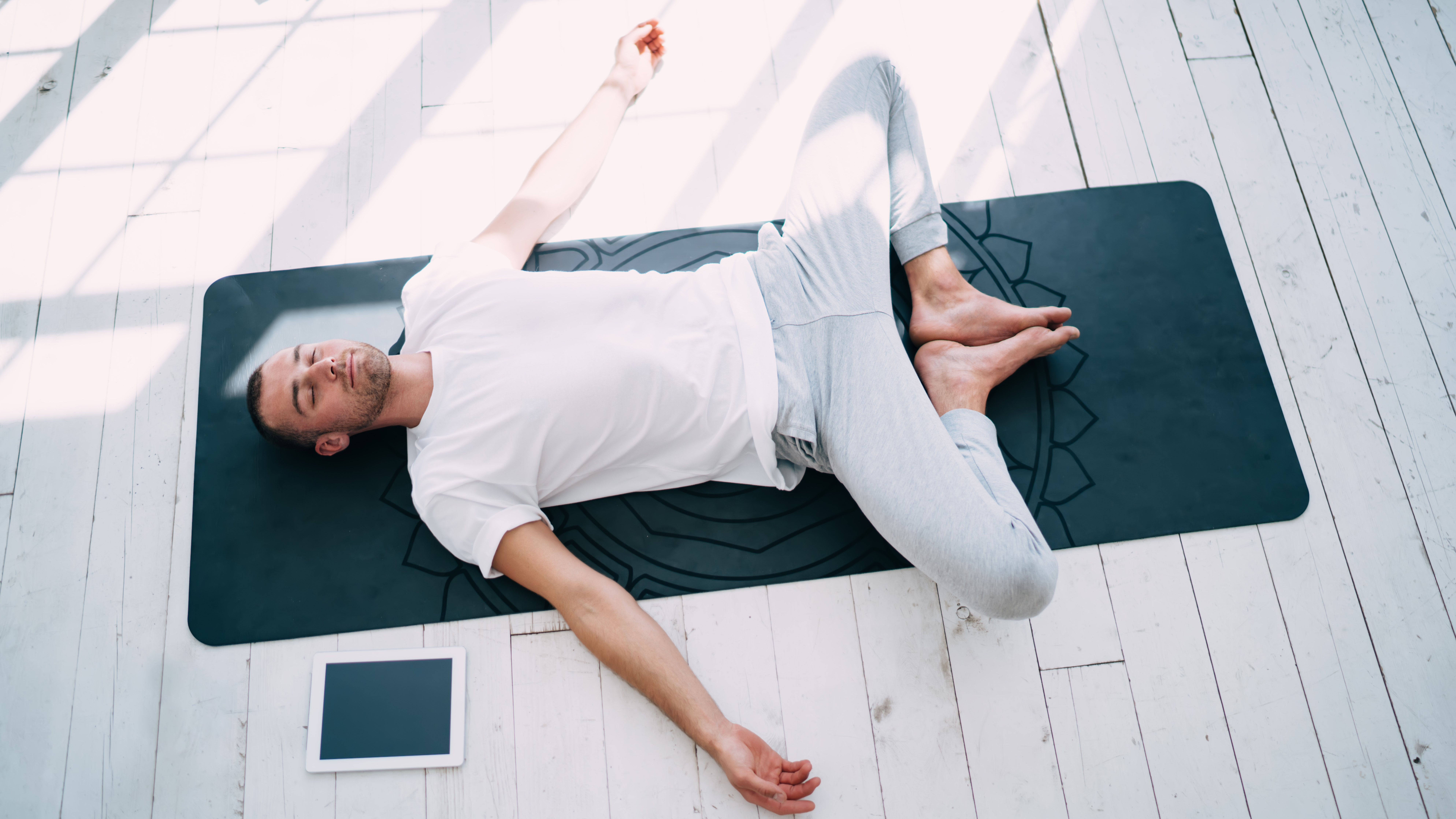 A man lies on his back performing butterfly pose. His knees are bent, feet touching, arms splayed out by his sides.