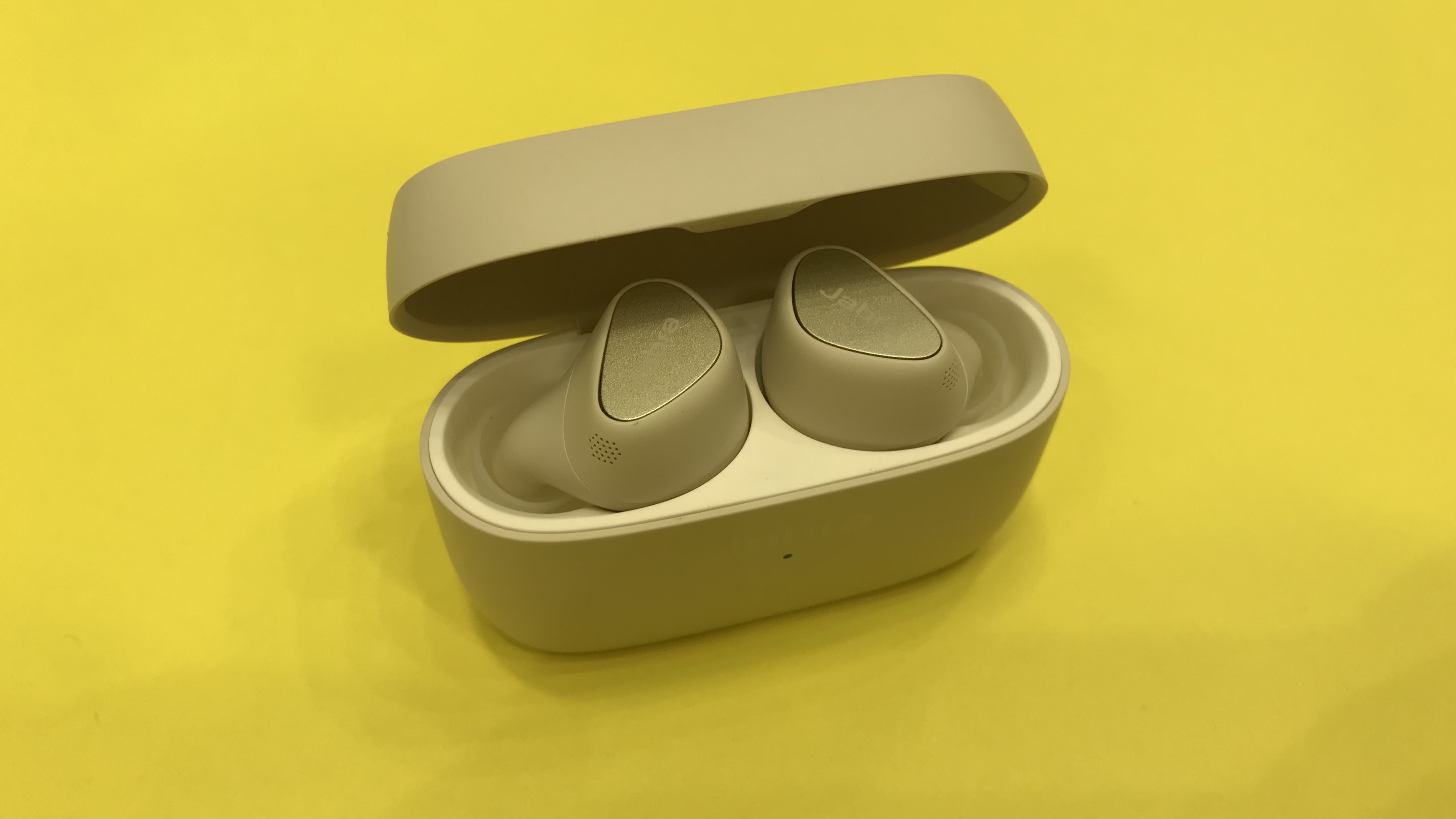 Jabra Elite 5 beige gold earbuds in charging case on yellow background