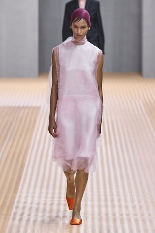 A model at Prada's spring/summer 2024 runway show wearing a pink sheer dress with orange square-toe mules.