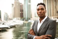 An attractive young businessman in a suit poses in front of a cityscape. 