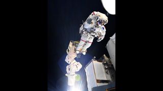 ESA astronaut Thomas Pesquet riding the space station's robotic arm during a space walk.