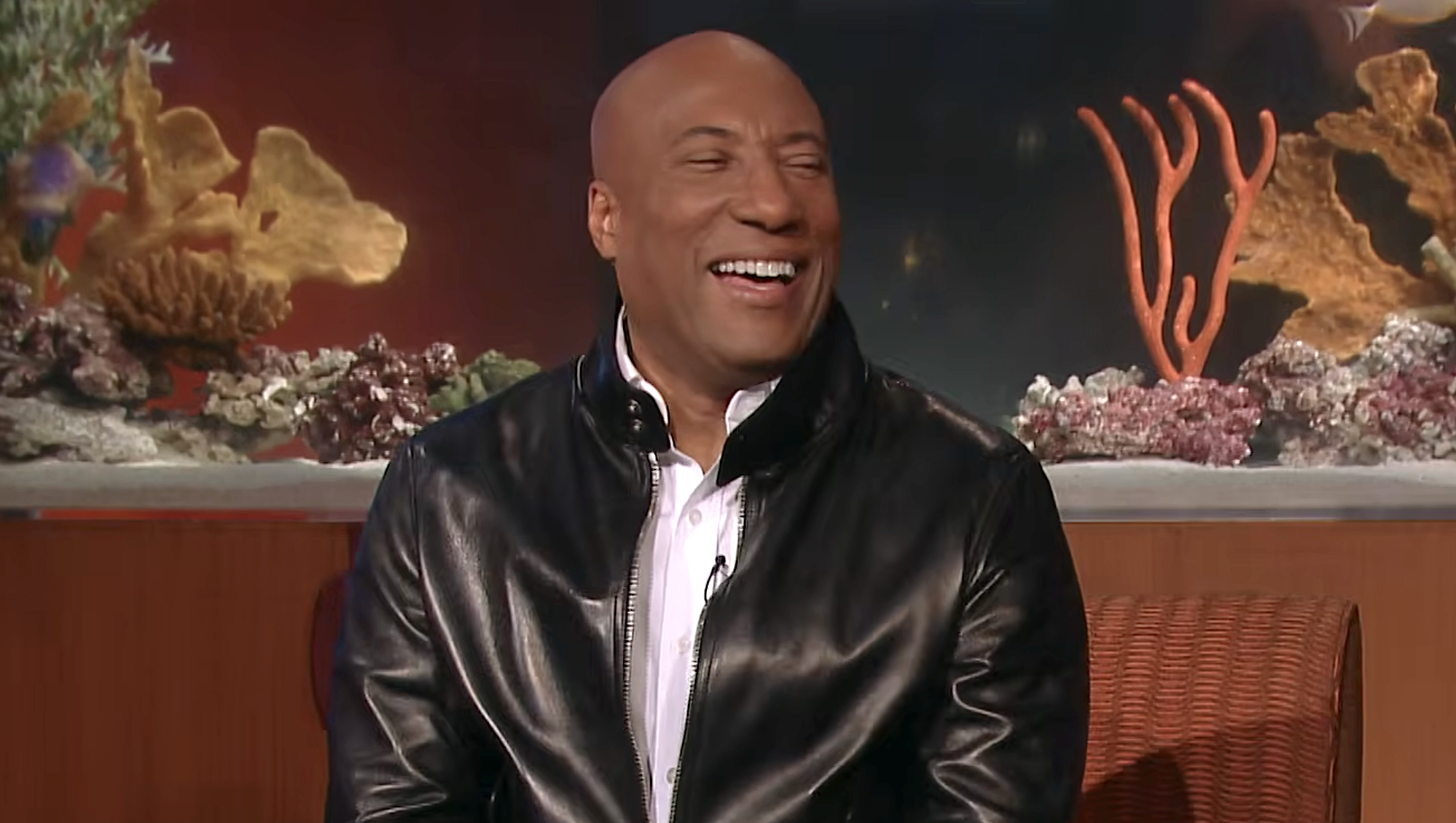Byron Allen in black jacket laughing on Comics Unleashed