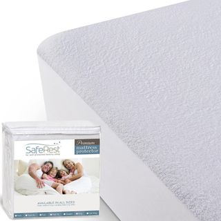 A white mattress protector on a bed with a folded one in white and plastic packaging 