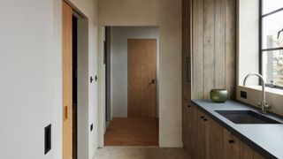 Minimalist modern utility room with natural wood cabinetry, sleek black worktops, and large window bringing in natural light. Neutral stone floor and timber accents create a calm, contemporary atmosphere.