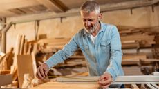 An older man measures a board for a project in his woodworking workshop.