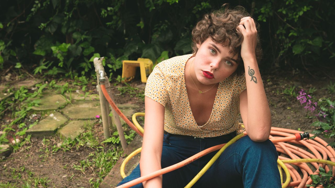 Garden hose being used by a woman looking glum