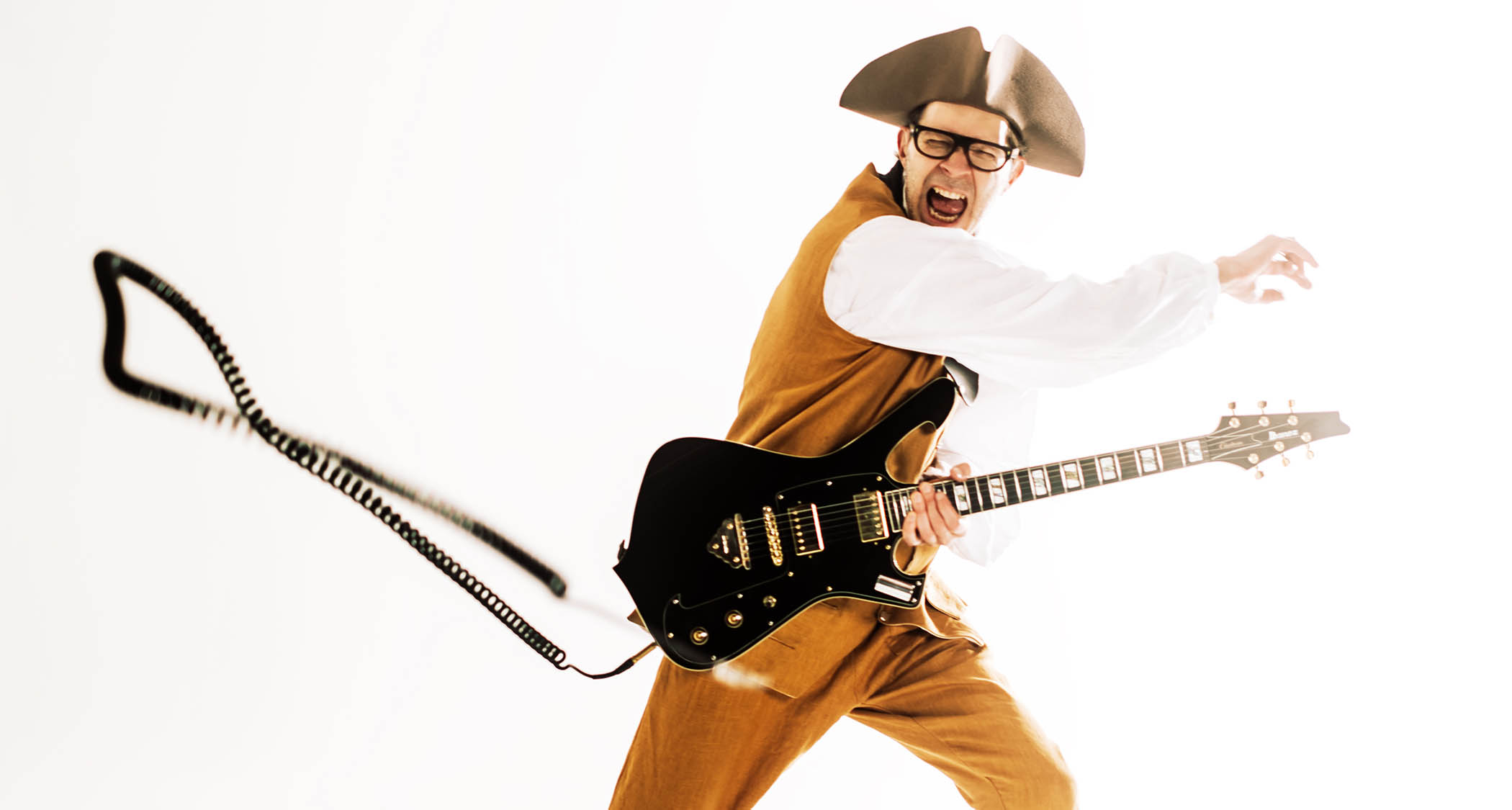 Paul Gilbert wears a tricorn and period dress as he poses in shred mode with his signature Ibanez guitar