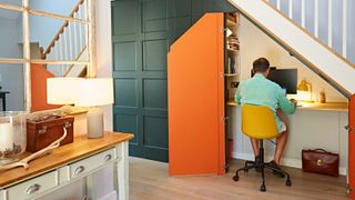 office under stairs with doors painted orange on the inside and man sat at desk working
