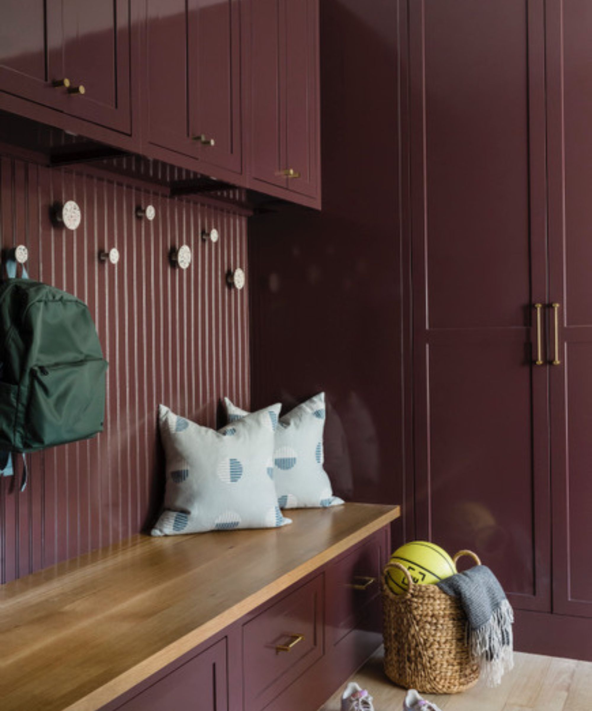 Mudroom with built-in bench and cabinets painted in aubergine with two pale blue cushions and a basket