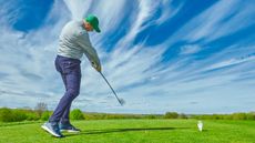 A golfer just after impact on a drive from behind