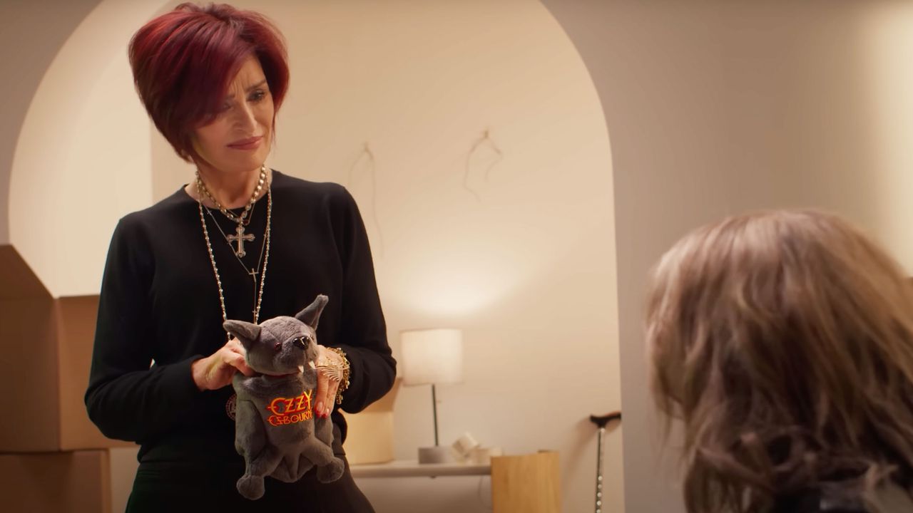A shot of Sharon Osbourne in a brightly lit living area holding an Ozzy Osbourne branded bat plush