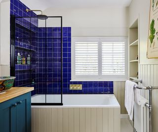 panelled bath with black metal shower screen and bright blue tiled section to wall behind and to side of shower