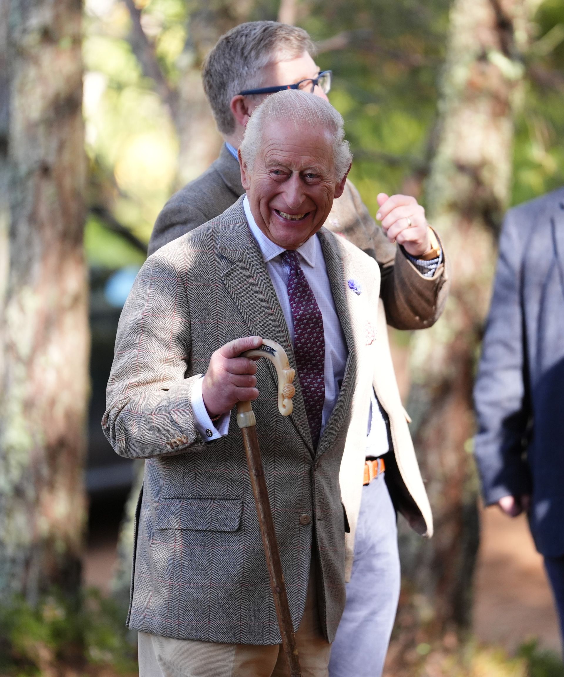 King Charles walking with a walking stick and laughing