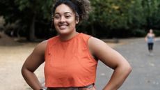 Portrait of smiling young woman standing on a road park and looking at camera. Curly hair. Sleeveless orange t-shirt.