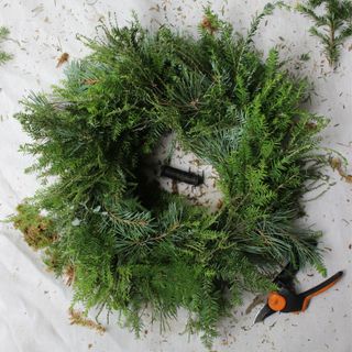 Black and orange secateurs next to wreath with fresh foliage