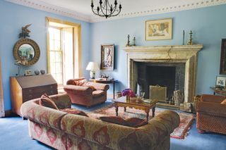 blue living room with tapestry style chairs and sofa and ornate fireplace