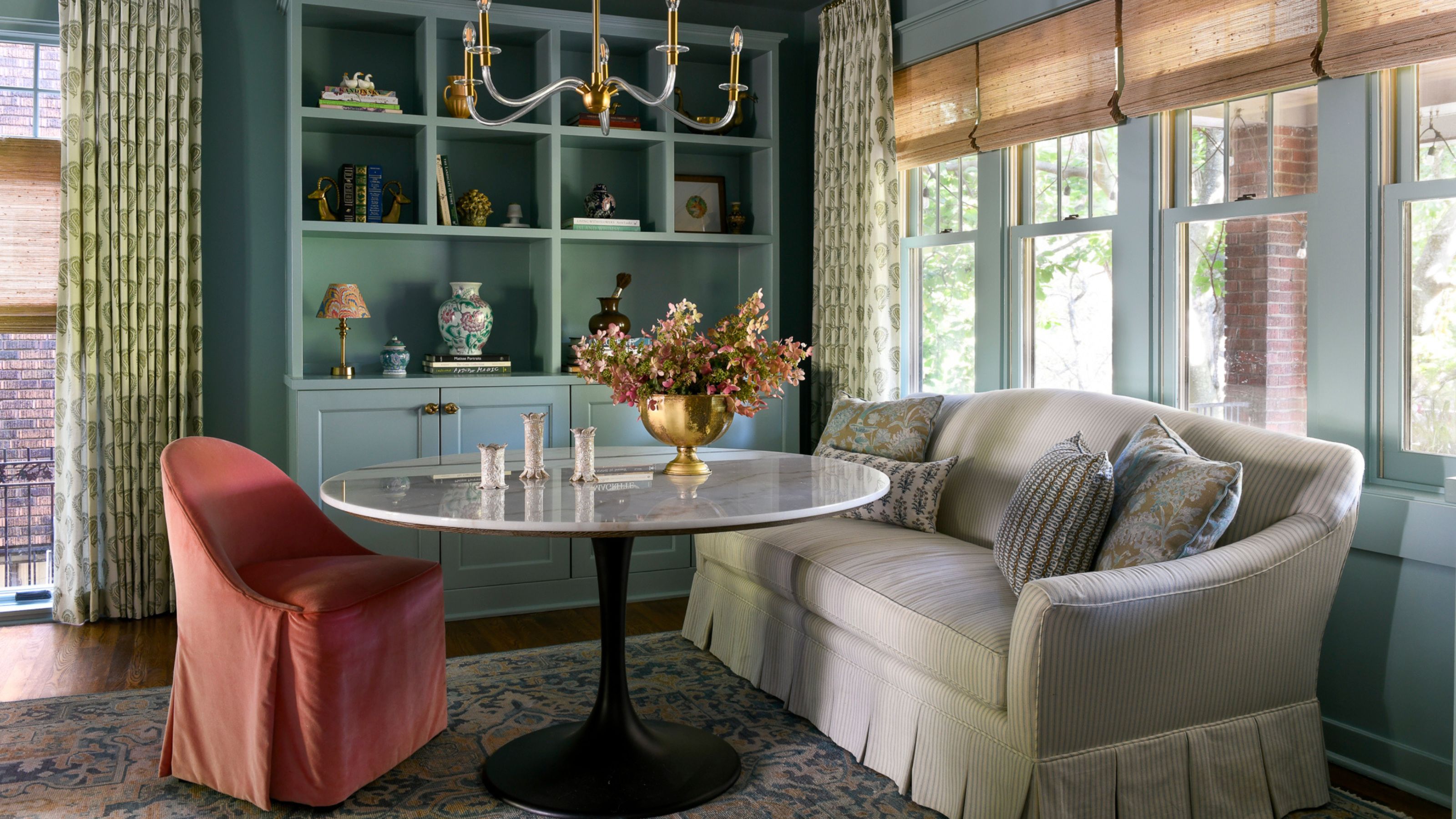A corner of a living room with light blue walls and built-ins, a ticking stripe sofa, and a pink chair with a round table.