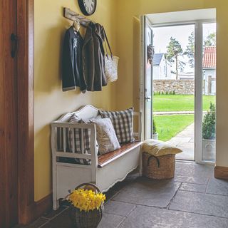 A yellow-painted hallway with a white bench with cushions and a storage basket