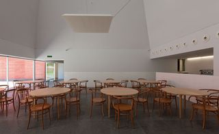 A cafeteria featuring white walls, white ceiling, grey flooring and clear glass panel with brown round table and matching chairs