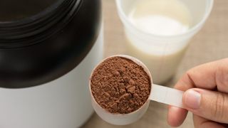 Protein powder in a measuring cup being poured into a protein shake