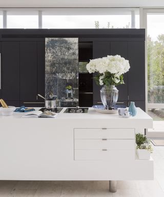 Glossy white kitchen island with hob and large bouquet of flowers