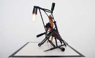 View of a light sculpture by Leo Capote - a dark sculpture made using various hand tools, metal and a bulb