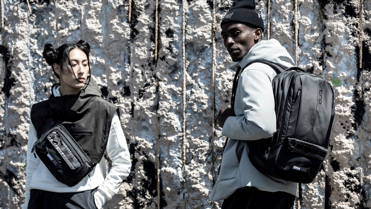 Two models with bags. Female model left of frame. Male model right of frame with backpack.