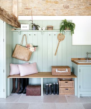 green boot room with exposed stone walls, green tongue and groove and wooden bench in 12th century Cotswolds country house