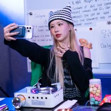 A content creator (Sia Jiwoo) takes a selfie in a streaming room with a whiteboard, on Netflix's 'The Influencer.'