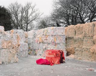 A large pile of hay bales are stacked one on top of each other. There are other material scraps next to them, with a red fabric in the center.
