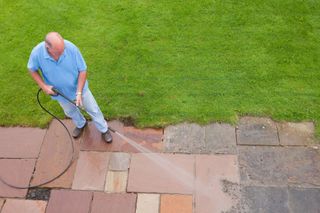 A man in a blue shirt wityh a pressure washer cleaning patio slabs