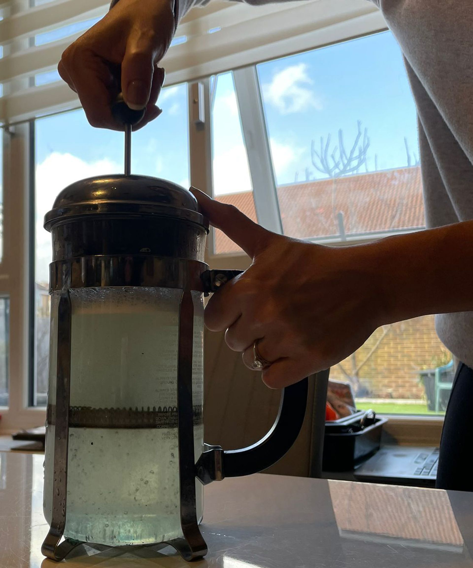 Christina Chrysostomou mencelupkan pembuat kopi pers Prancis di dapur putih