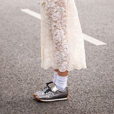 A street style image of a stylish person wearing silver sneakers with white socks and a white lace skirt.