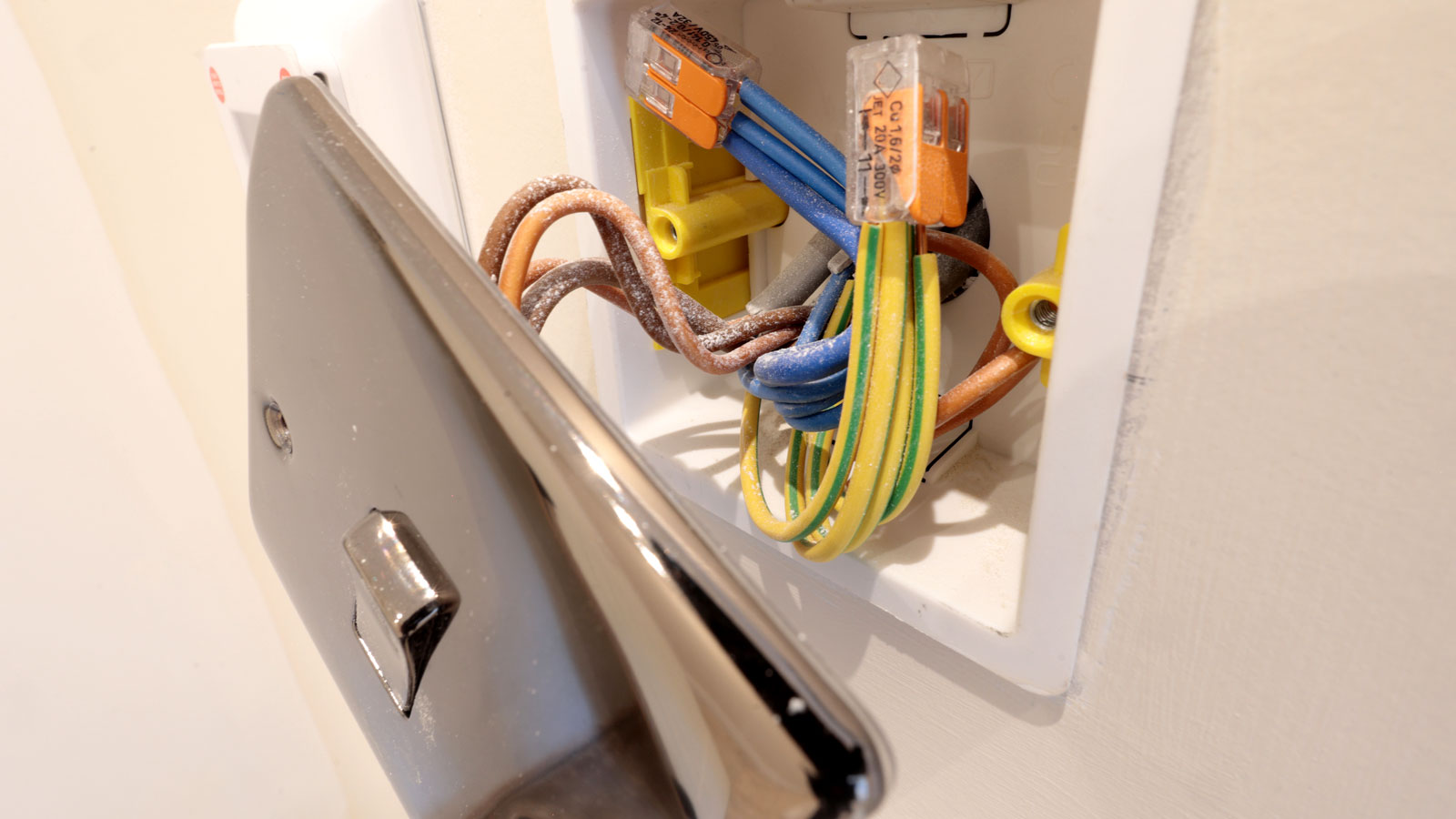 Close up of chrome single switch light switch cover attached to back box with brown, blue and green/yellow wiring