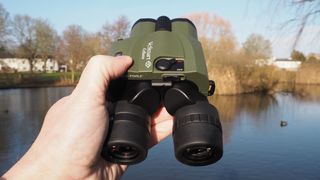 Kenko VC Smart Cellarto 10x30 WP binoculars held in a hand outside in front of a lake