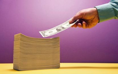 Man's hand placing 1 US dollar bill on large piles of bill on yellow shelf, purple background, selective focus
