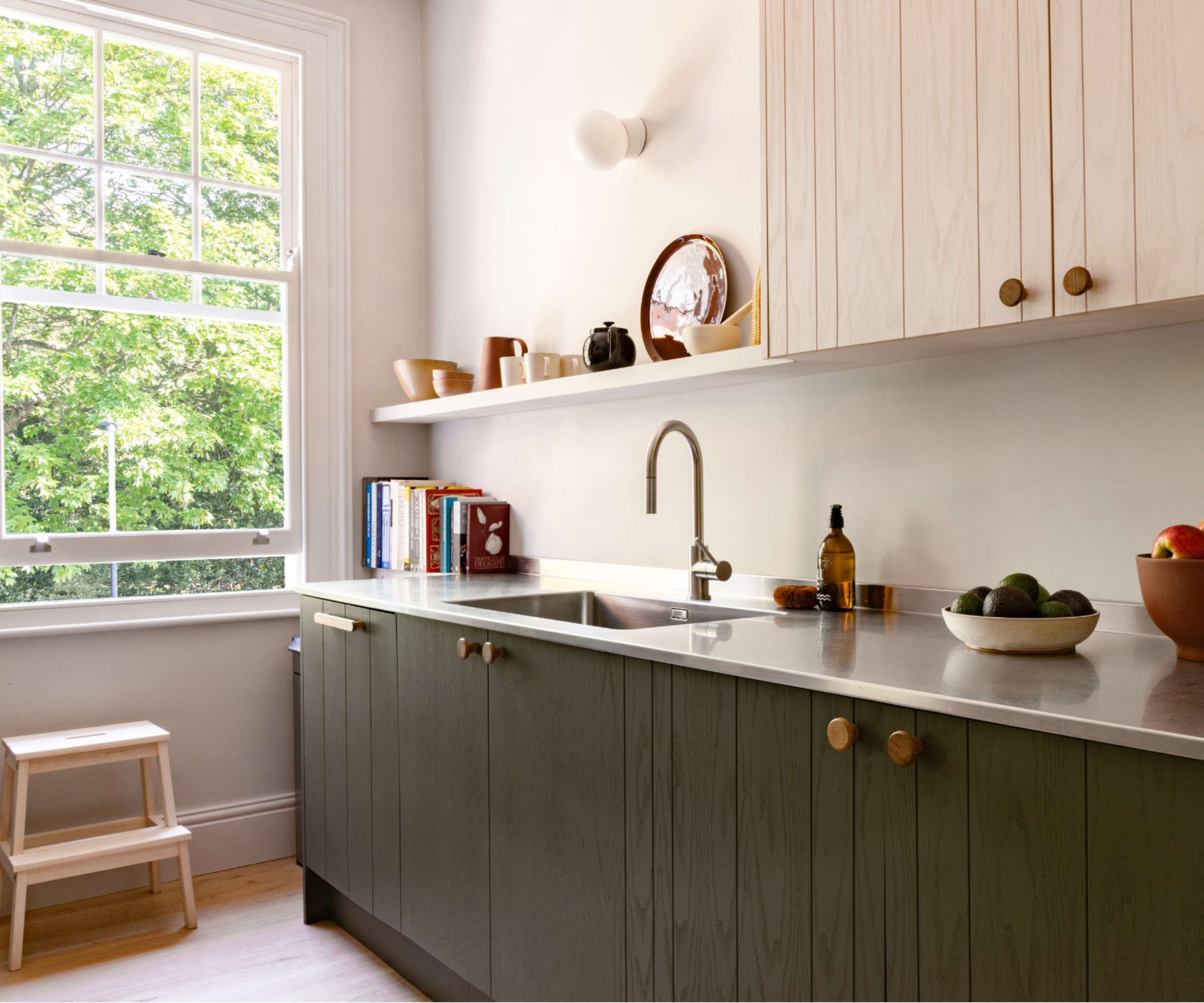 galley kitchen with green and pale wood slatted cabinets, stainless steel worktop, open shelving and large sash window