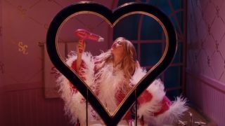 Sharpay singing signing into a hair dryer from behind a heart shaped mirror.