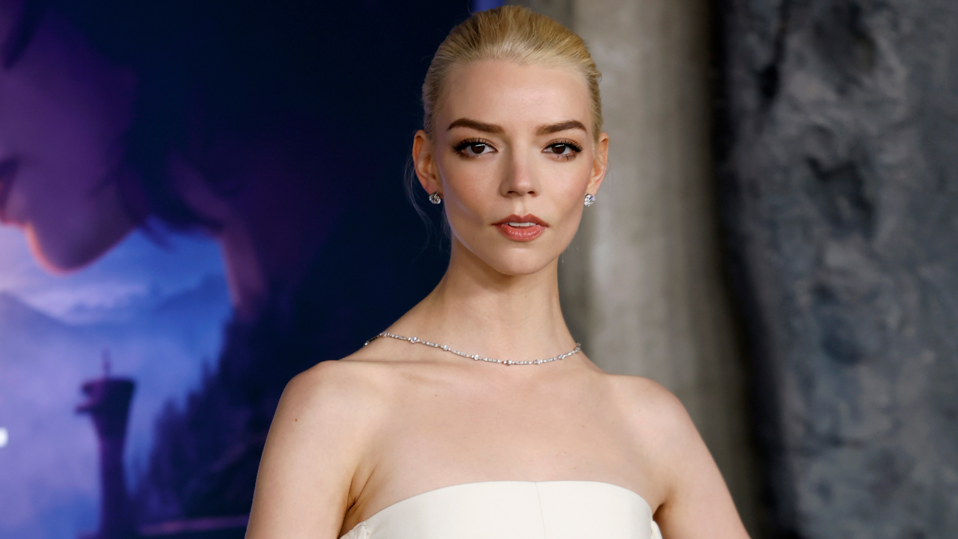 Anya Taylor Joy with her blonde hair pulled into an updo hairstyle. She&#039;s wearing a strapless white dress and a necklace. 