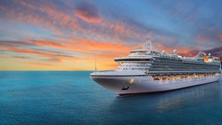 A cruise ship on the ocean water with a sunset in the background