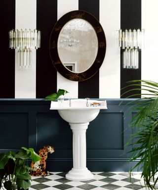 black and white striped wallpaper on wall behind white sink with wood panelling on lower half