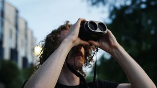 A man looking through the Fujifilm Techno-Stabi TS-L 1640 image-stabilized binoculars upwards with trees and buildings in the background.