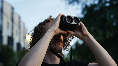 A man looking through the Fujifilm Techno-Stabi TS-L 1640 image-stabilized binoculars upwards with trees and buildings in the background.