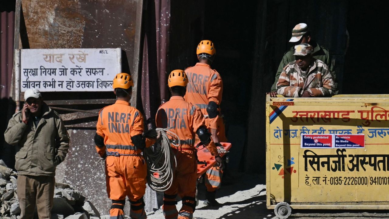 Rescue workers in orange jumpsuits and helmets at the entrance to the Silkyara road tunnel