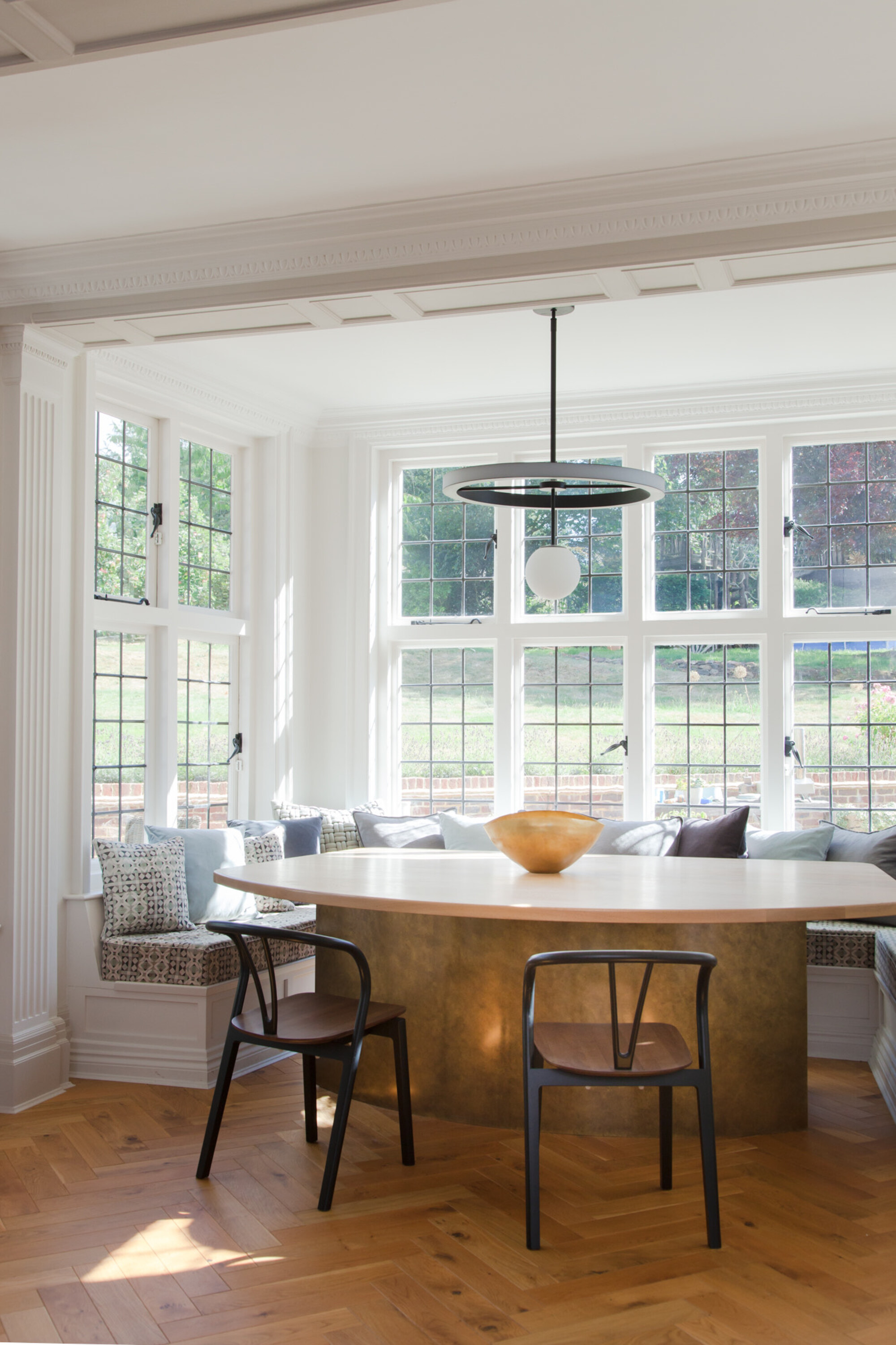 window seat dining area, modern brass table with upholstered seat and cushions, and two wishbone chairs, parquetry floors, and pendant light overhead