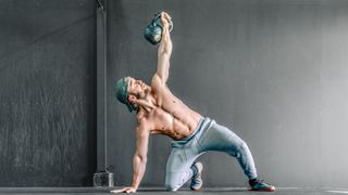 a topless man performing kettlebell windmills on the floor