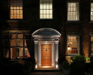 An example of front porch lighting ideas showing an illuminated porch with a wooden front door and sash windows