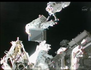 Astronauts Sunita Williams and Akihiko Hoshide hold power unit during spacewalk.