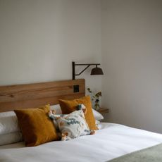 A white-painted bedroom with a wooden bed and contrasting scatter cushions on top